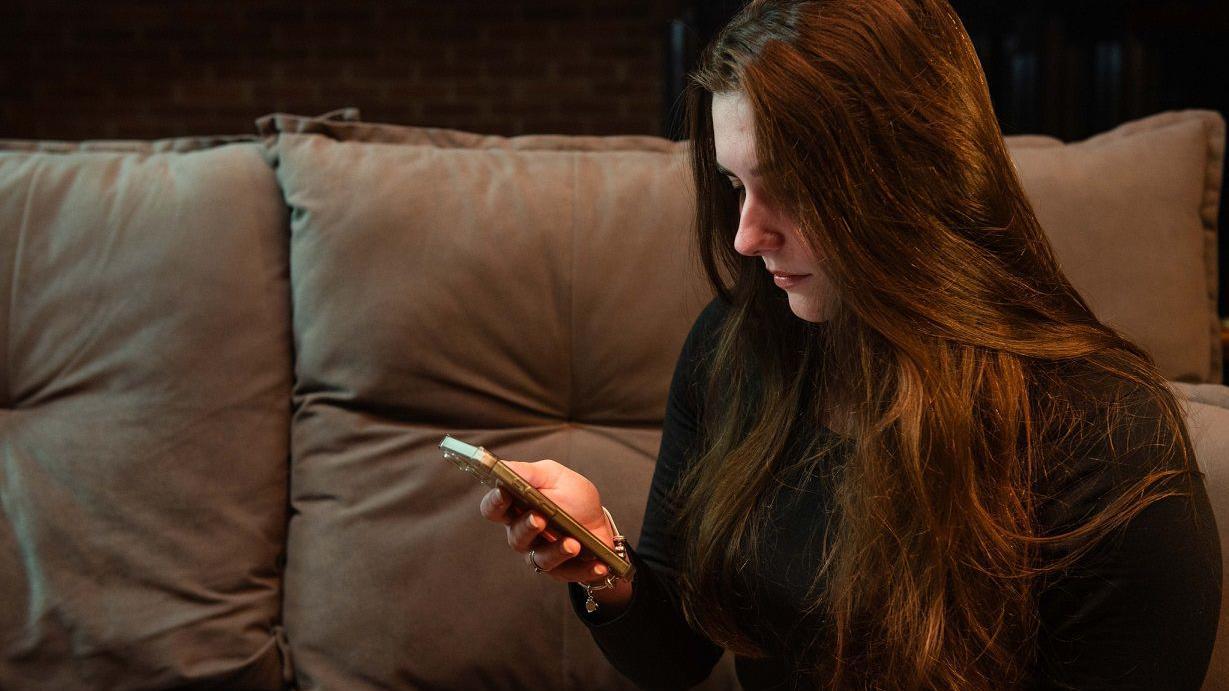 Michele no sofá olhando para celular