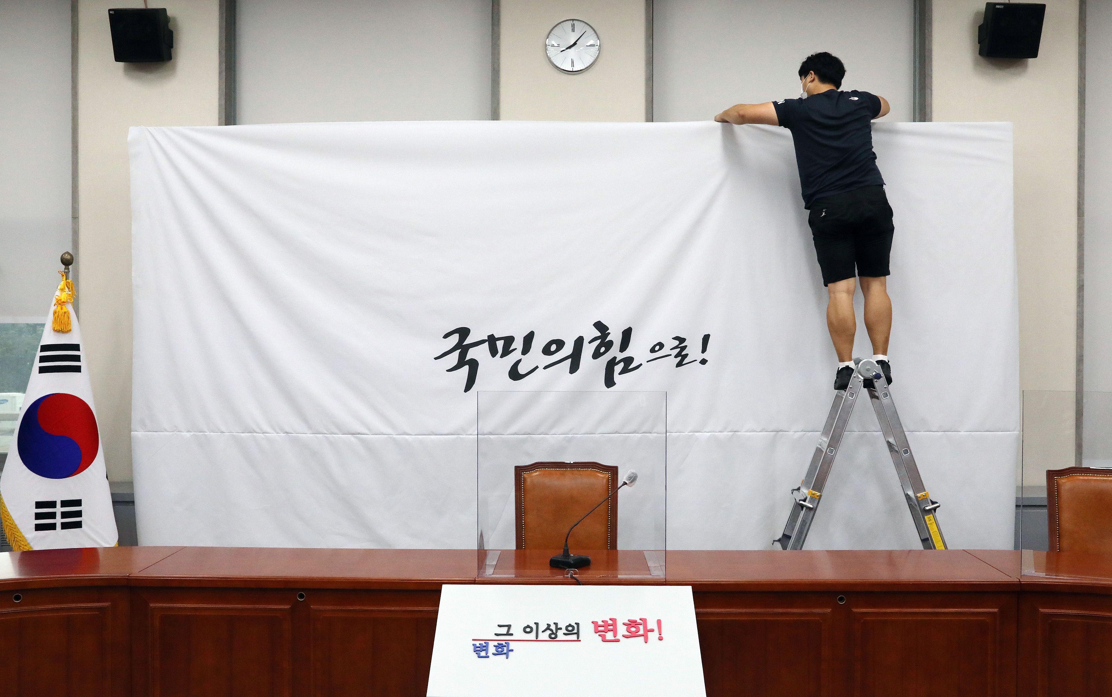지난 2020년 3월 당명을 '미래통합당'에서 '국민의힘'으로 변경한 국민의힘 담당자가  서울 여의도 국회 당대표회의실의 백드롭 교체 작업을 하고 있다. 배경에는 '국민의 힘으로'라는 글씨가 보인다.