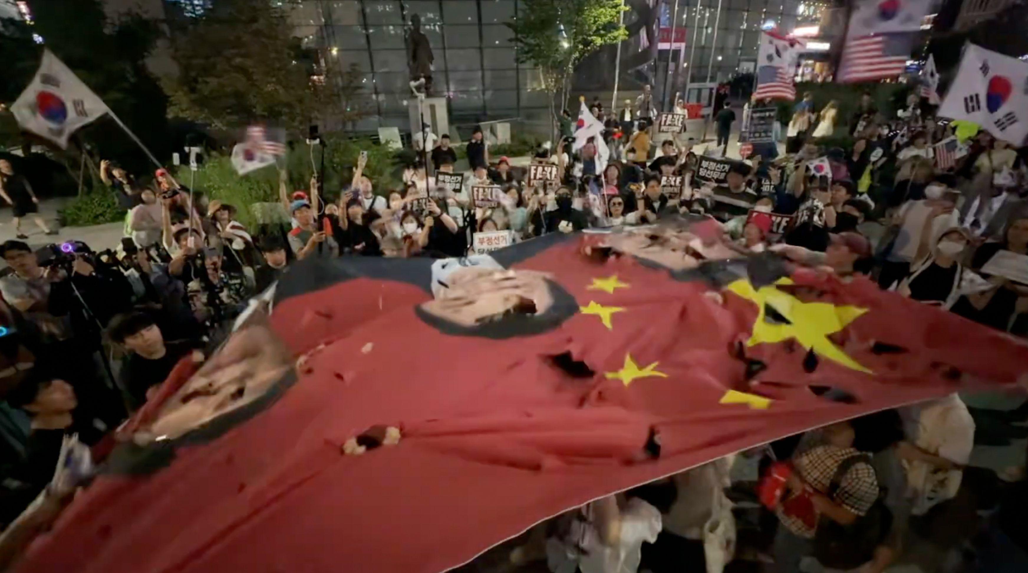 韓國首爾梨泰院一場由「自由大學」組織的反華集會上,示威者撕毀一面印上了習近平和其他中國主要官員照片的巨型中國國旗(BBC韓語圖片18/10/2025)