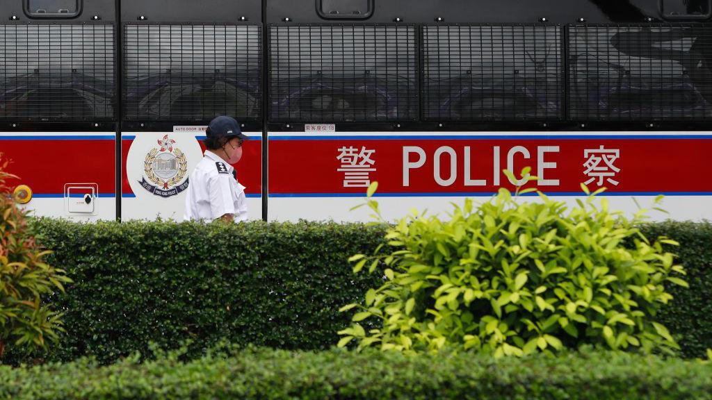 2023年6月24日，一辆警车在香港维多利亚港执勤，一名警员在警车前走过。
