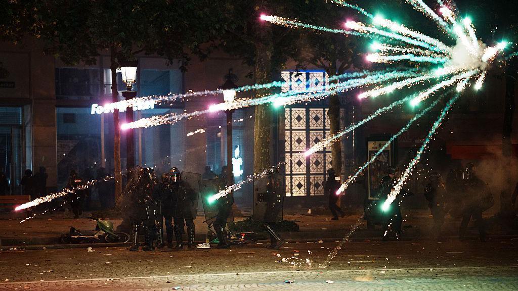Unos policías se resguardan de unos fuegos articiales que fueron lanzados en su contra.