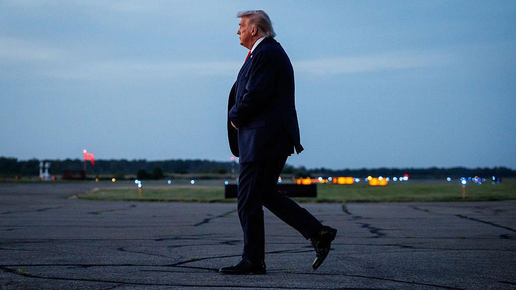 Donald Trump, visto de perfil, caminhando sozinho na pista de um aeroporto.