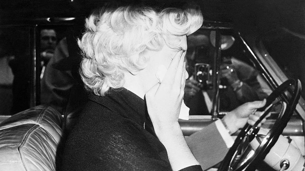 Marilyn Monroe en un auto se lleva las manos a la cara, con tristeza, tras la separación de Joe DiMaggio