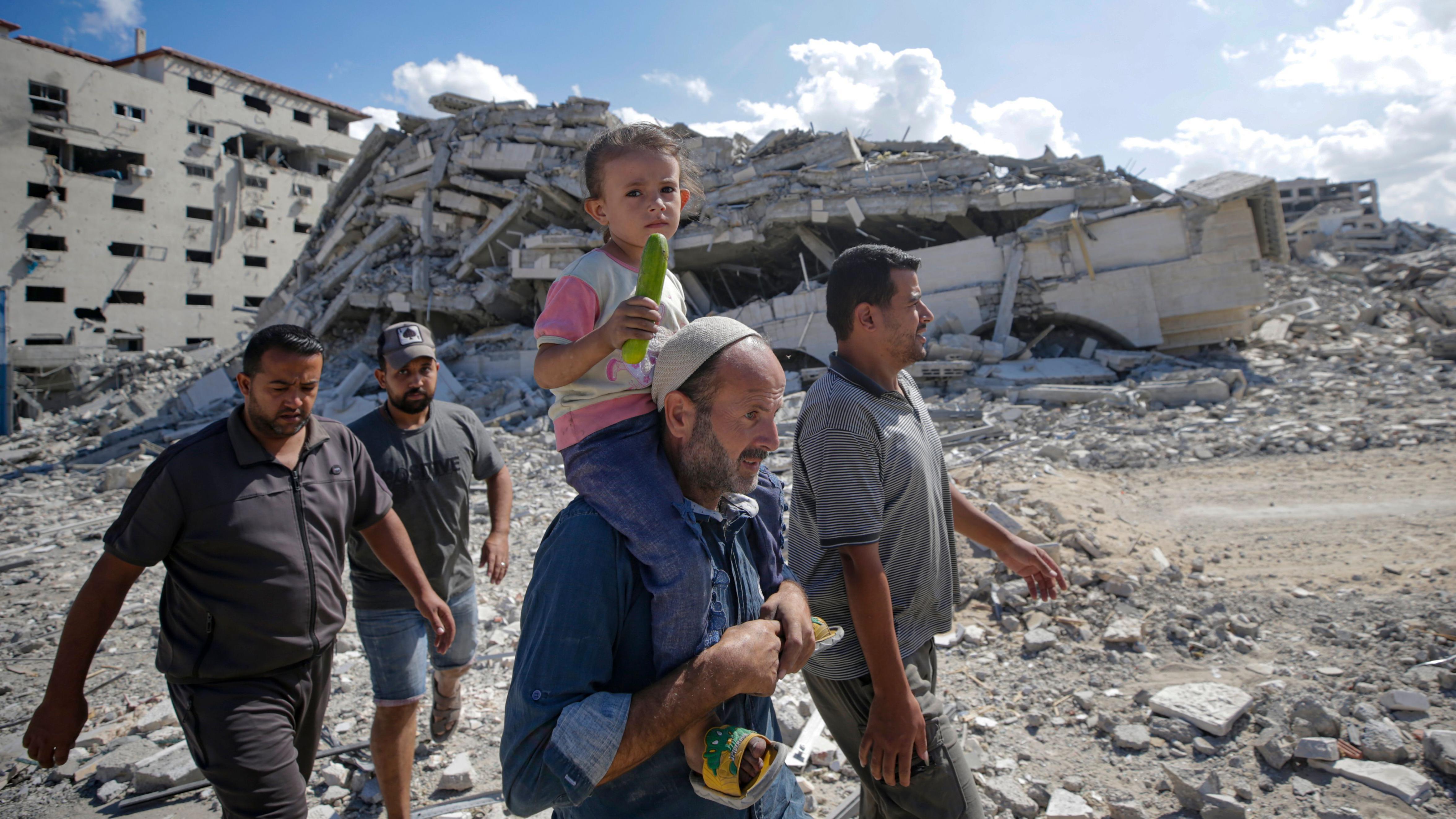 Varios hombres, uno de ellos con un niño a hombros, caminan entre los escombros en la Franja de Gaza en octubre de 2025