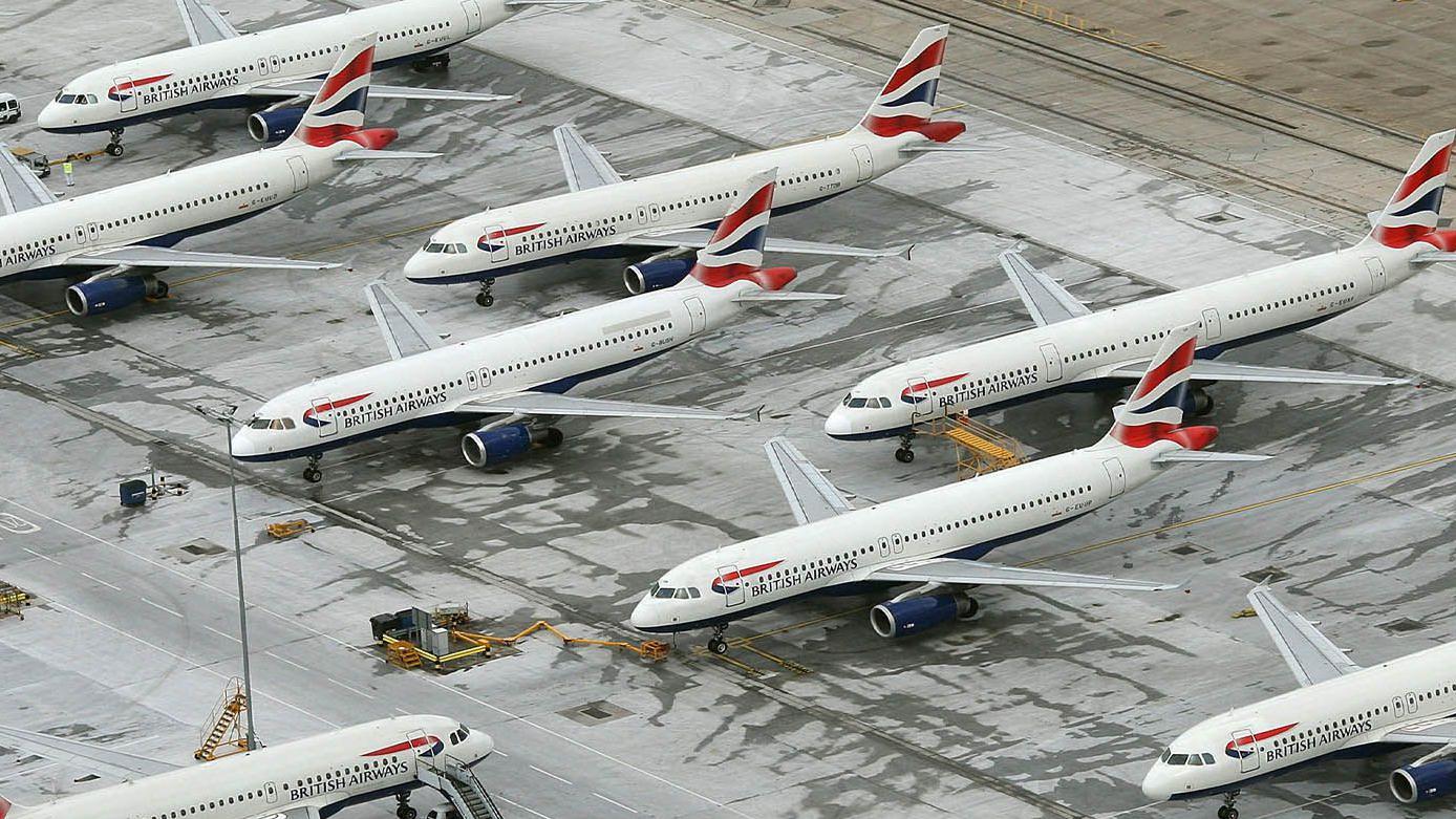 Vista a&eacute;rea de um grupo de avi&otilde;es da British Airways estacionados em fileiras, com as aeronaves pr&oacute;ximas entre si e equipamentos de servi&ccedil;o ao redor 