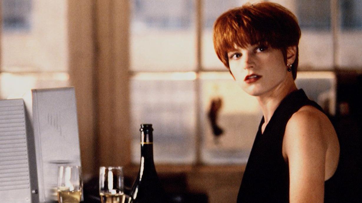 Bridget Fonda com cabelo curto vermelho, usando blusa preta