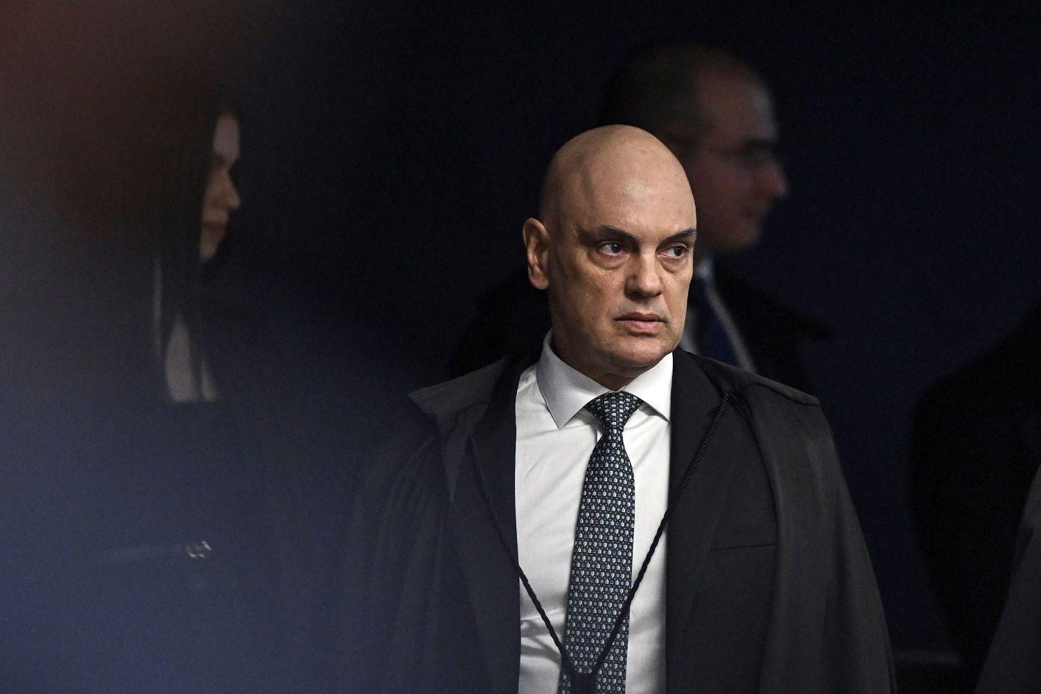 Moraes com olhar sério, caminhando, com outras pessoas no plano de fundo 