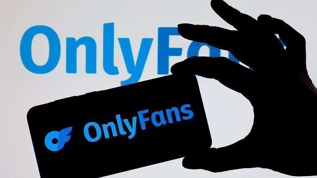 Uma m&atilde;o segurando um celular com o logo do OnlyFans.