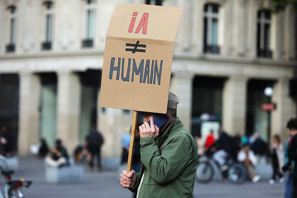 رجل يرفع لافتة مناهضة للذكاء الاصطناعي دفاعًا عن العمل البشري، وذلك خلال تجمع في باريس، فرنسا، في 22 مايو/ أيار 2025. وجاءت هذه الفعالية للدفاع عن مؤدّي الأصوات ضد المخاطر التي يطرحها الذكاء الاصطناعي.