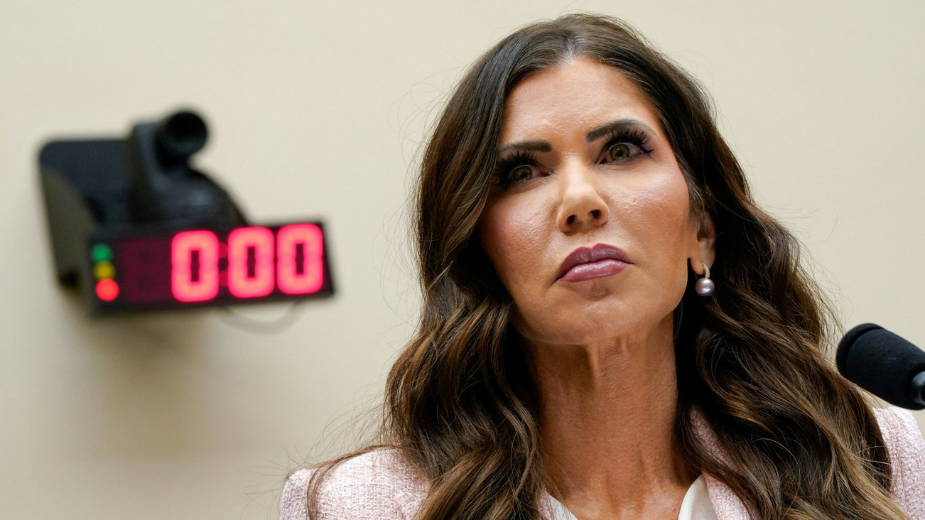 Kristi Noem ispred mikrofona gleda u daljinu u belom sakou