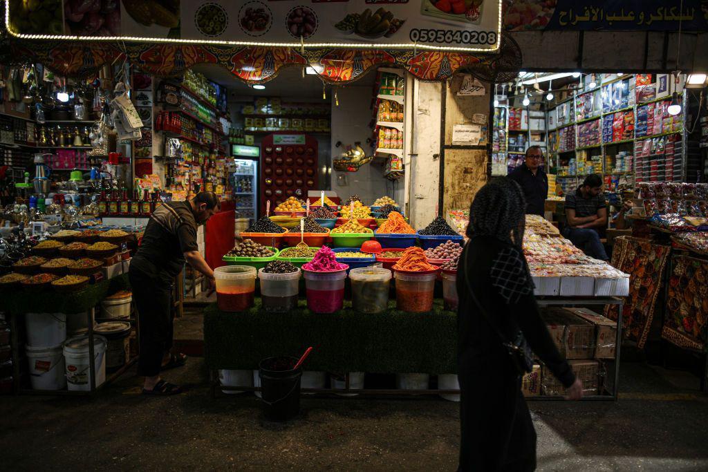 بقالات في سوق الزاوية القديم في مدينة غزة، سيدة تمشي أمامهم، ويظهر وجود الطعام بشكل واضح