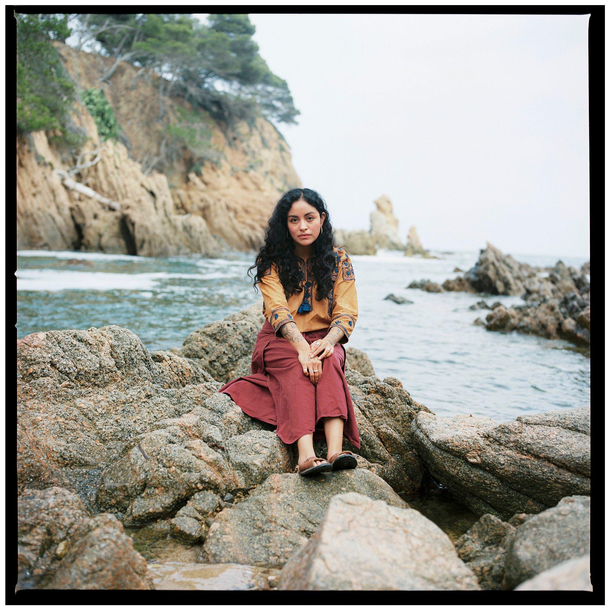 Retrato de Clyo Mendoza sentada en una piedra en una playa.