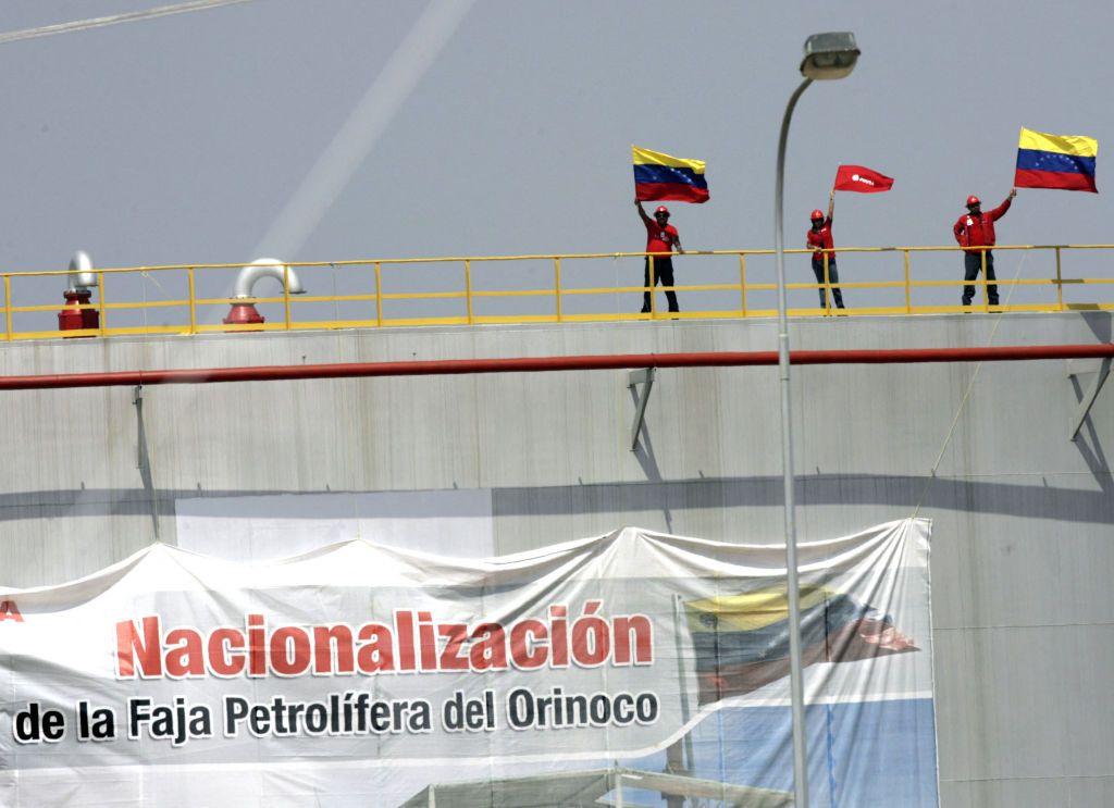 Trabajadores petroleros ondean banderas de Venezuela en la cima de un tanque de petróleo en el que hay una gran pancarta que celebra la "nacionalización de la Faja Petrolífera del Orinoco".