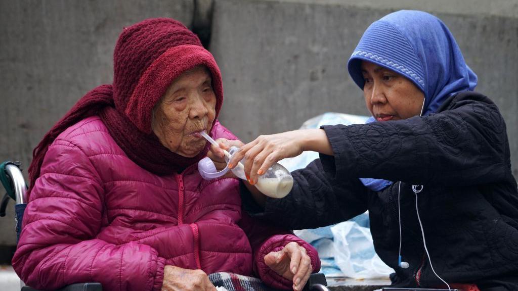 一名外傭正餵老人喝奶。