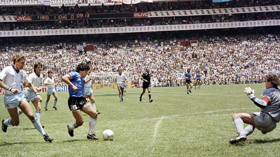 Se ve a Maradona regateando el balón a través de varios futbolistas ingleses y se ve al portero inglés lanzándose hacia un lateral.