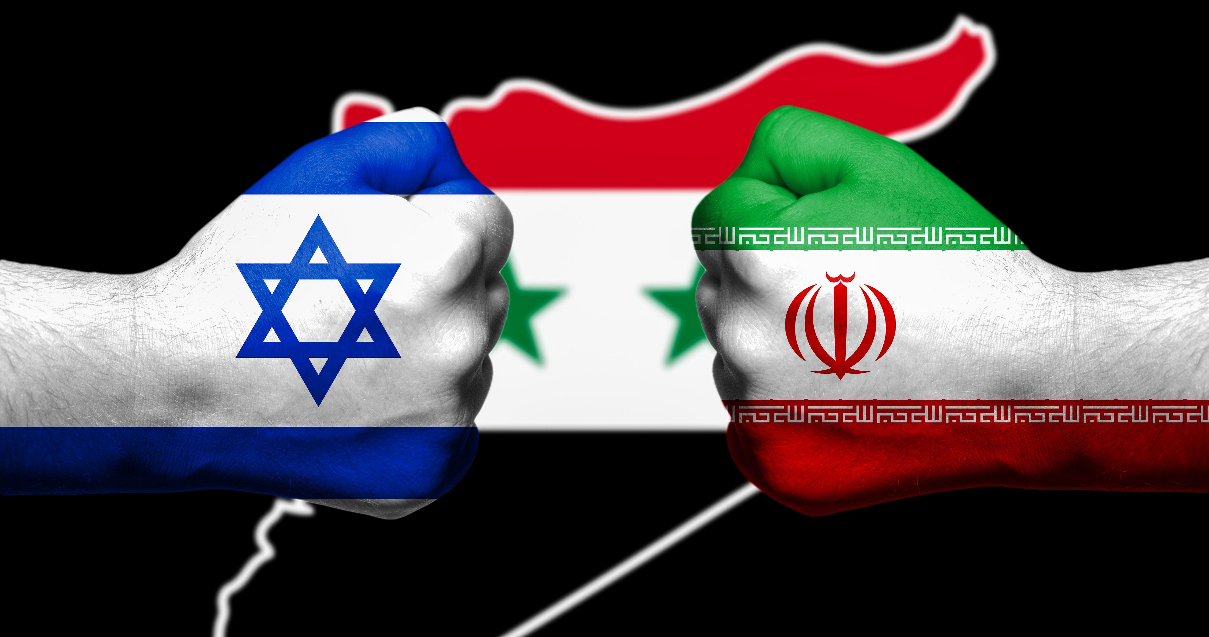 قبضتان مطليّتان بألوان العلمين الإيراني والإسرائيلي تتواجهان، وبينهما خريطة سوريا بألوان العلم السوري