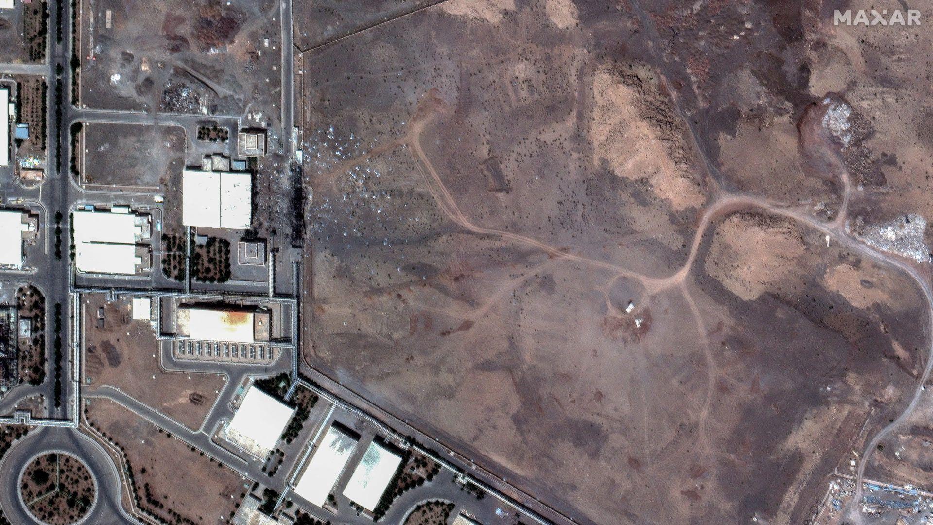 منطقة سوداء مليئة بالأنقاض بجوار مبانٍ في منطقة نطنز. تمتد شبكة من الطرق المستقيمة بين المباني، مع وجود دوار أسفل يسار الصورة.