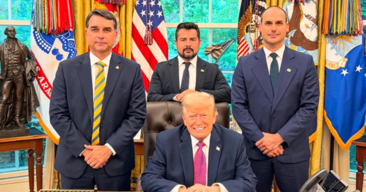 Foto do senador Flávio Bolsonaro, Donald Trump (sentado), Eduardo Bolsonaro (do lado direito) e Paulo Figueiredo sentado atrás de Trump. Todos no salão oval da Casa Branca.