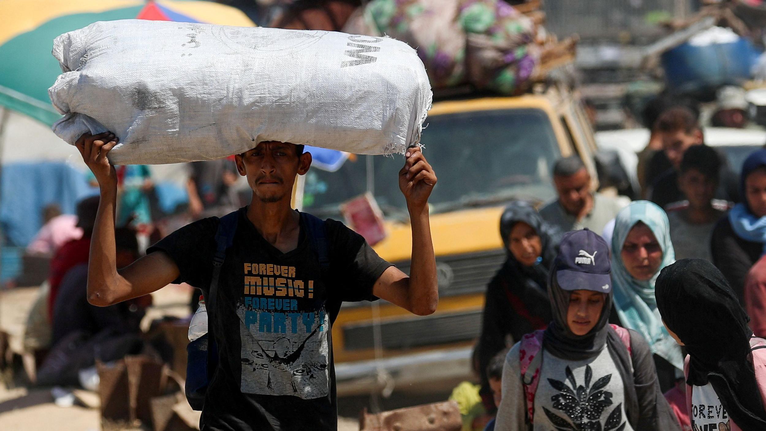 Personas huyen del asalto israelí a gaza. En primer plano se ve a un hombre con un costal sobre su cabeza. Un niño camina a su lado. 