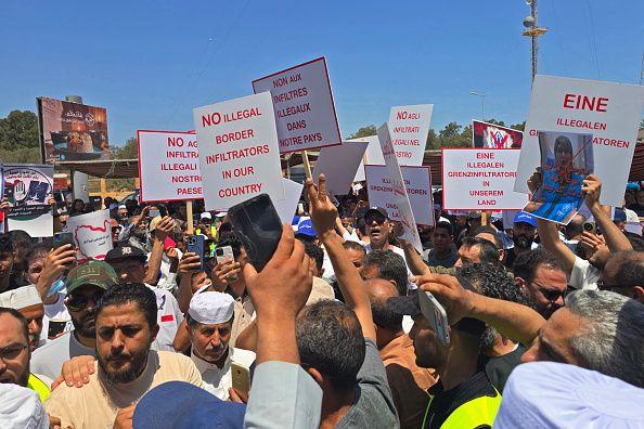 حشد من الناس، غالبيتهم رجال، يرفعون لافتات، منها لافتة كتب عليها No illegal border infiltrators in our country "لا متسللين غير شرعيين عبر الحدود في بلادنا"