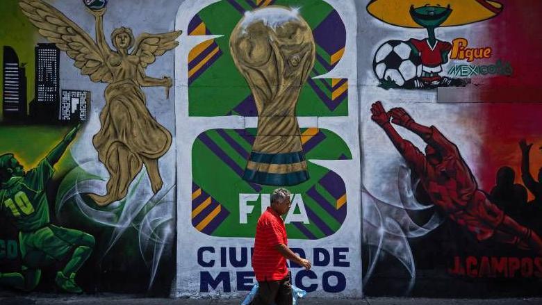 Un hombre con camisa roja camina frente a un mural en la Ciudad de México anuncia la llegada de la Copa Mundial de 2026, que se celebrará conjuntamente en México, Estados Unidos y Canadá.
