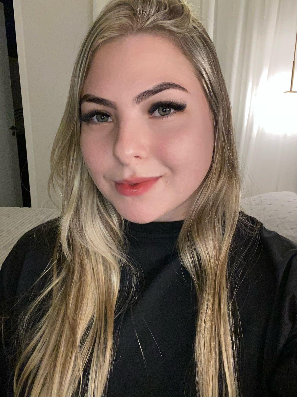 Raphaela em 'selfie'. Ela &eacute; loira, tem olhos azuis, e olha diretamente para a c&acirc;mera, com um sorriso sutil.