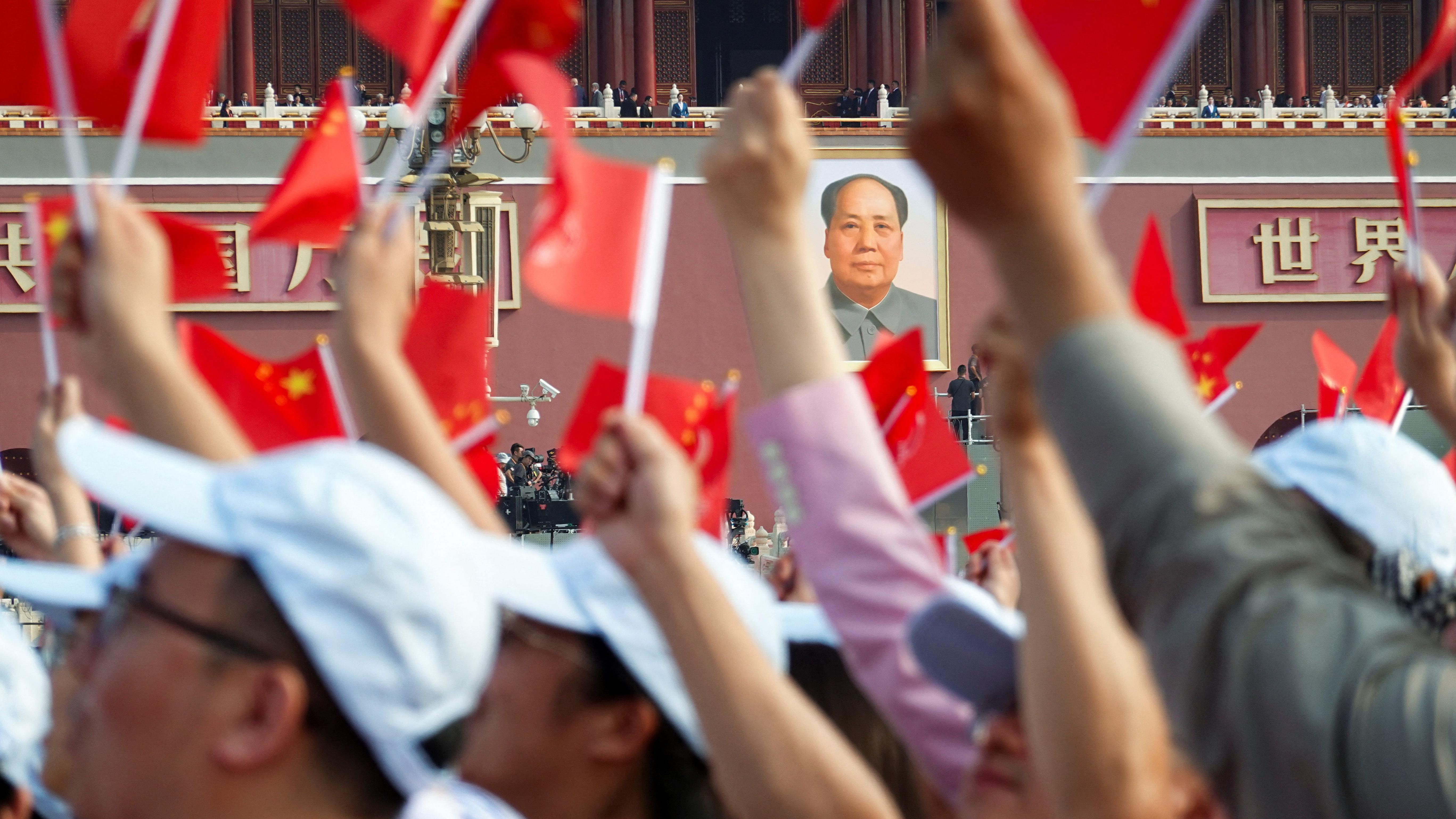 Un retrato gigante del difunto presidente chino Mao Zedong cuelga de la Puerta de Tiananmén mientras la gente ondea banderas antes de un desfile militar.