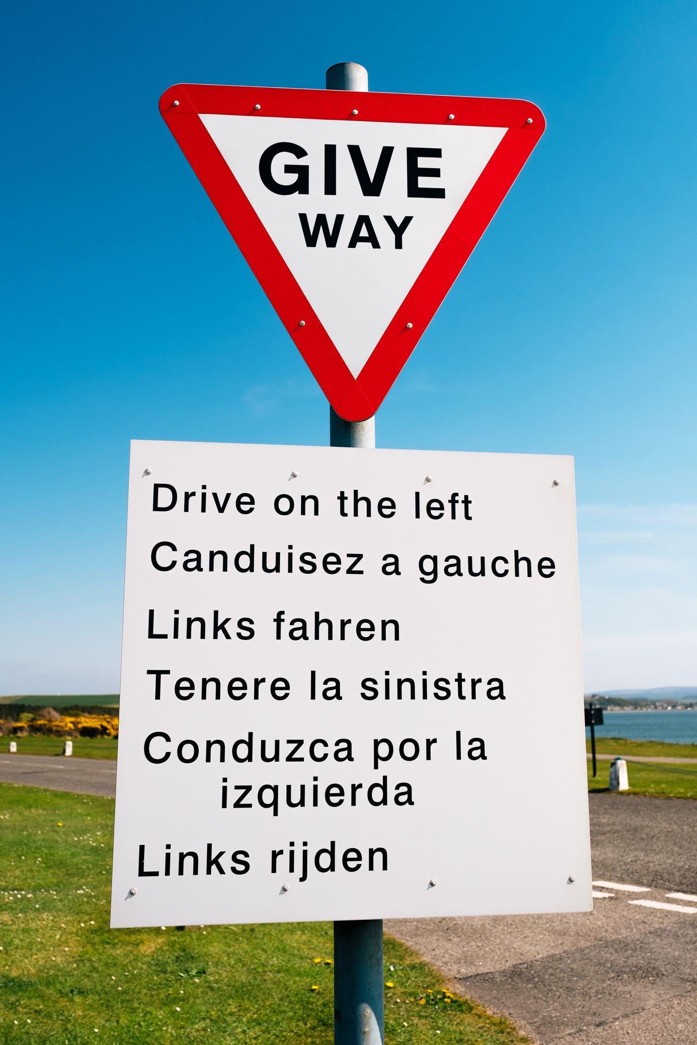 Placa de trânsito orientando as pessoas a trafegar pela mão inglesa, em seis idiomas