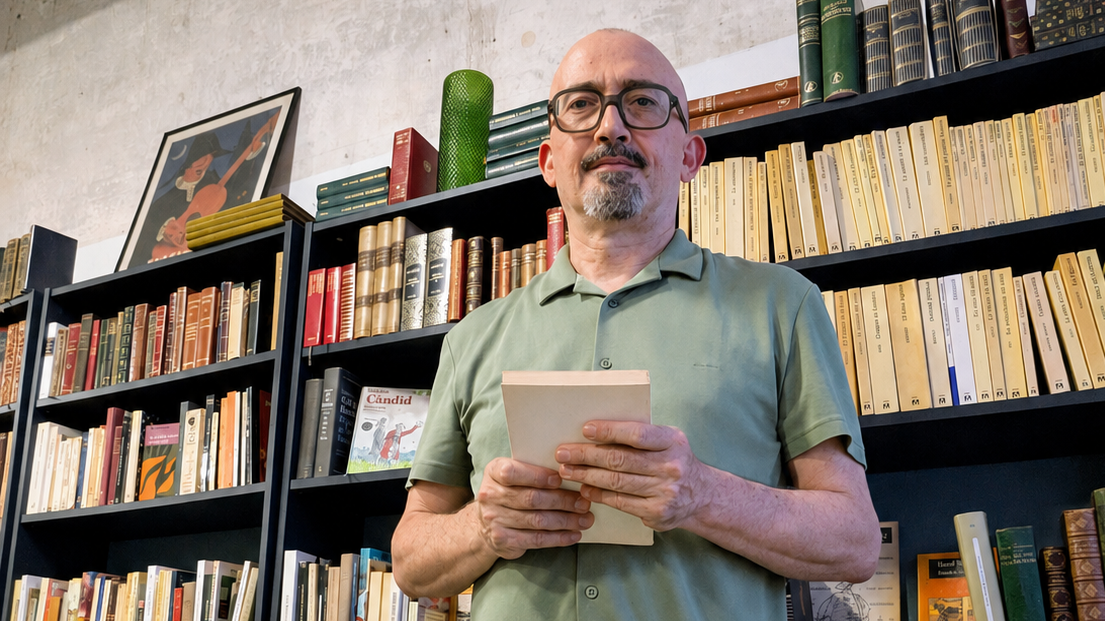 Un hombre sostiene un libro con una biblioteca detrás.