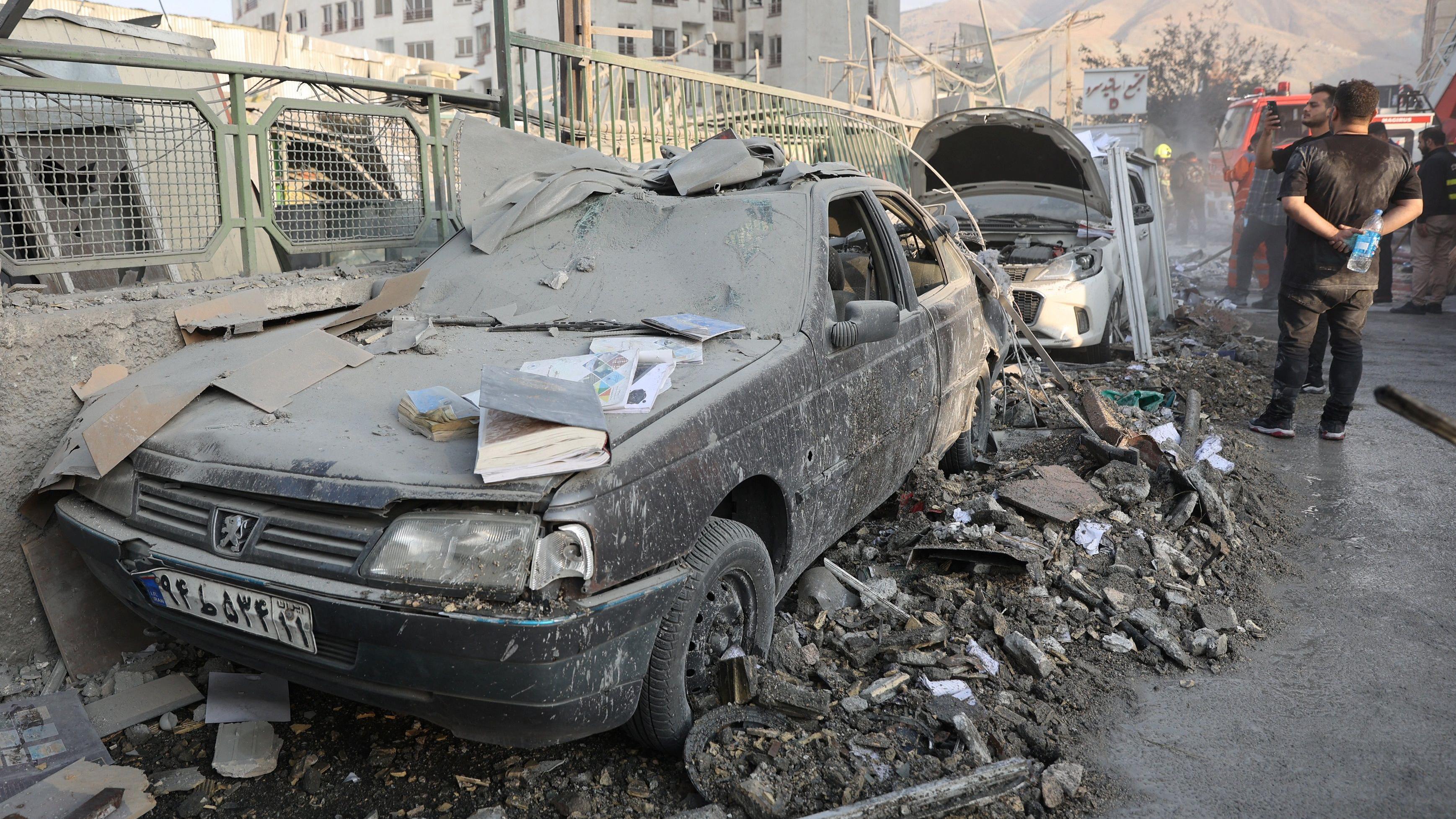 Carros cobertos por escombros nas ruas, com pessoas passando ao lado