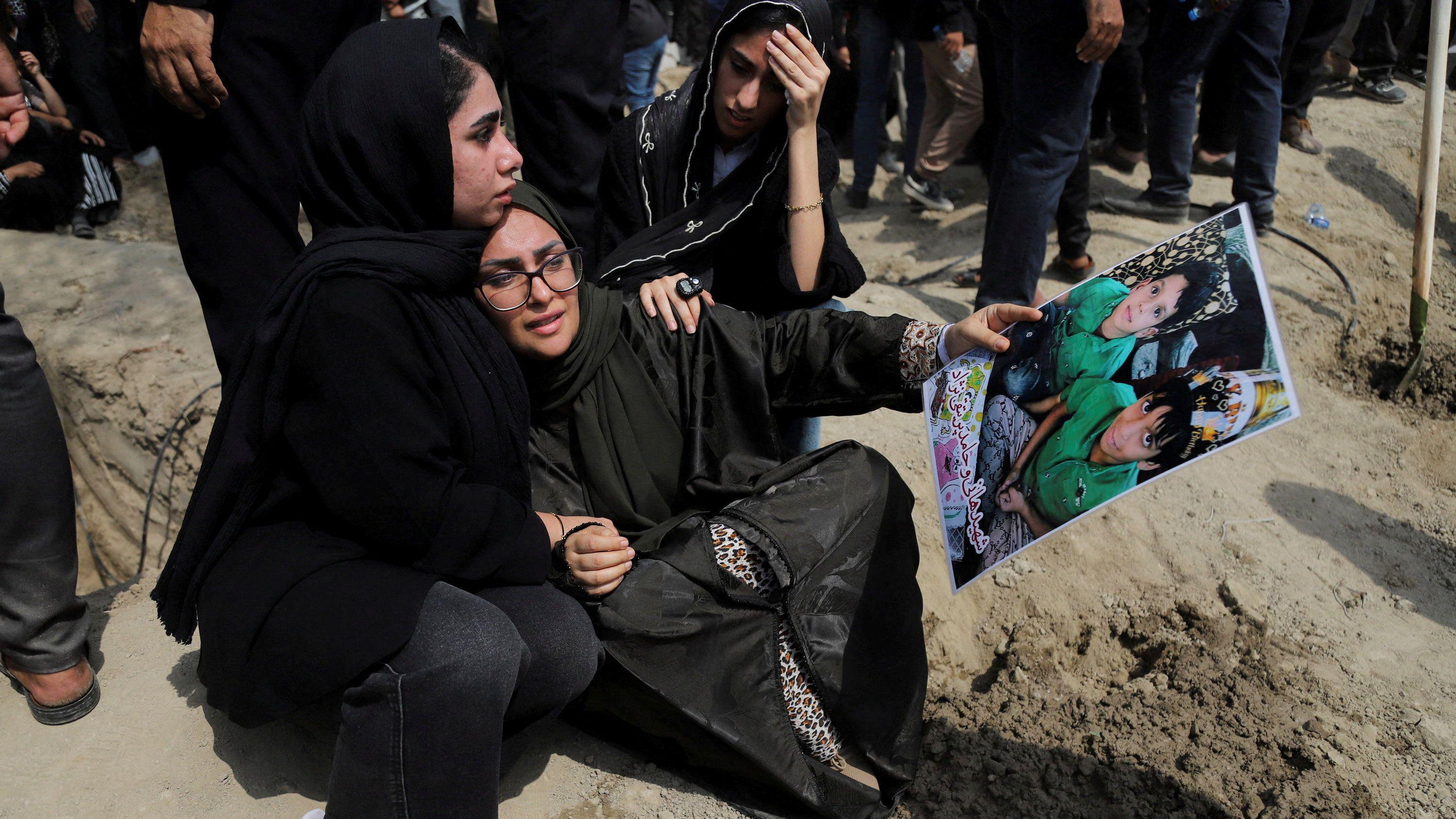 Dve žene u crnom plaču nad rakom, jedna drži fotografiju dvoje dece