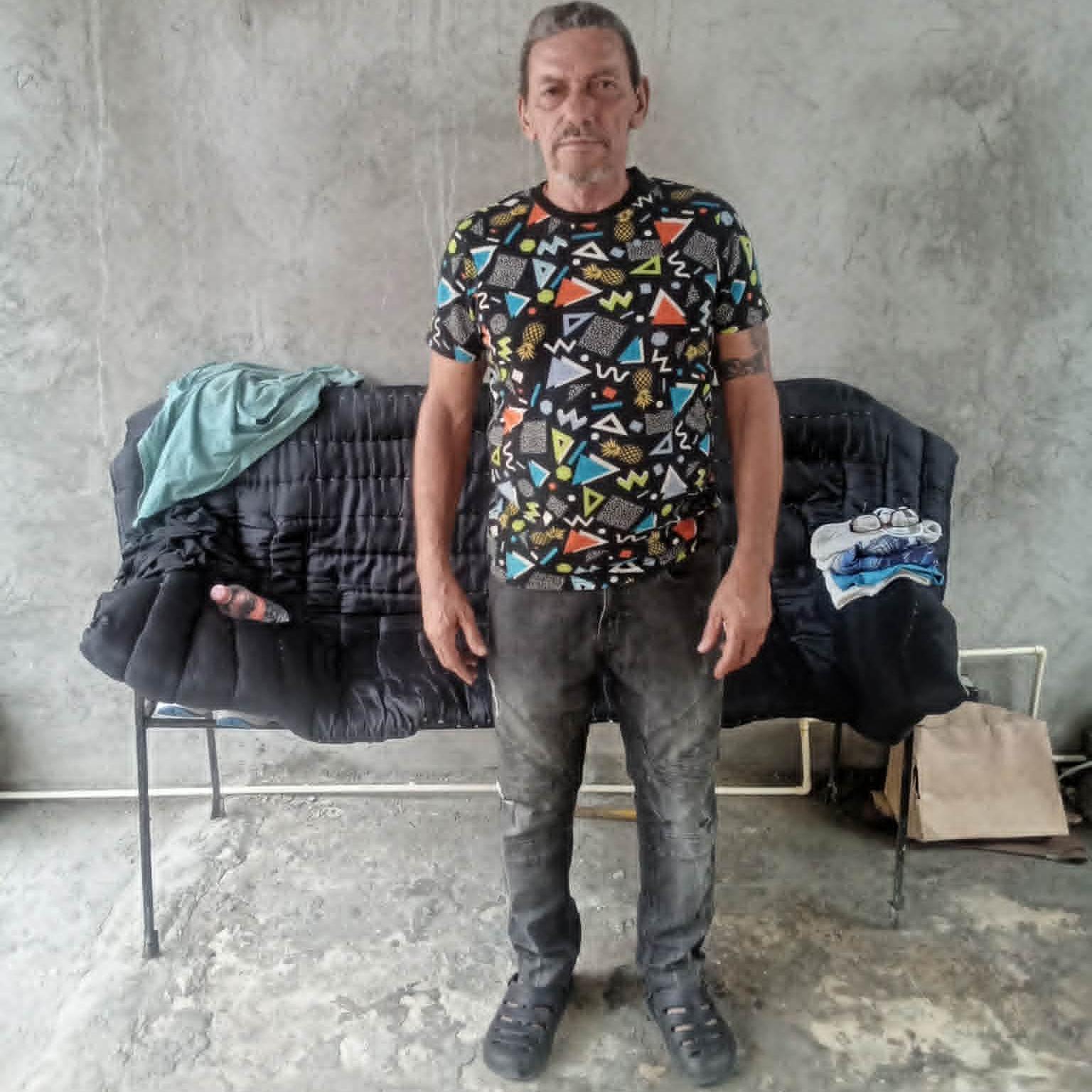 L&aacute;zaro Romero Le&oacute;n, de p&eacute;, olha para a c&acirc;mera em frente a um pequeno sof&aacute;, com jeans escuro e uma camiseta estampada, em um p&aacute;tio de cimento na cidade de Tapachula, no Estado mexicano de Chiapas