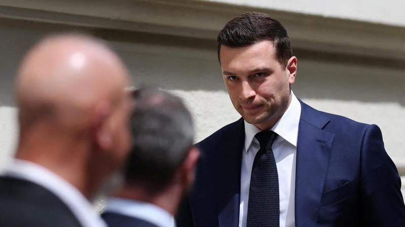 Jordan Bardella, de saco azul oscuro y corbata negra, tiene una expresión seria a la entrada al tribunal de apelaciones.