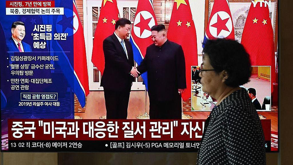 Una mujer pasa junto a una pantalla de televisión que muestra un noticiero con imágenes de archivo de la reunión de 2019 entre el presidente chino Xi Jinping y el líder norcoreano Kim Jong Un, en una estación de tren de Seúl el 8 de junio de 2026. 
