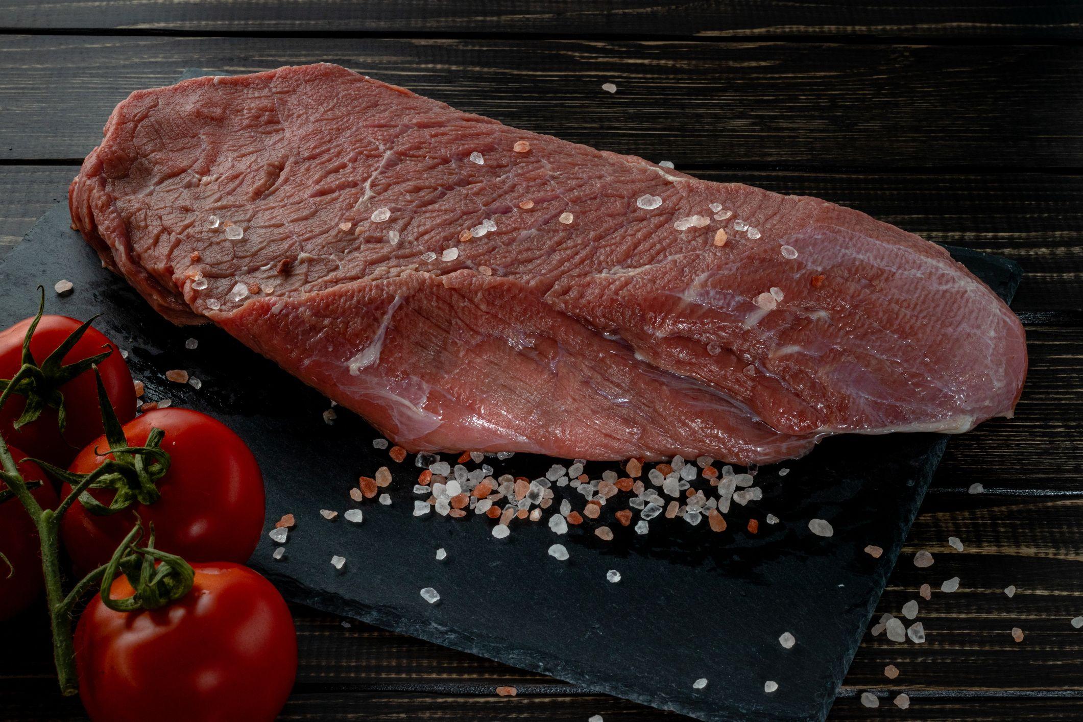 Filete de carne cruda con especias sobre un fondo de pizarra oscura, piedra u hormigón.