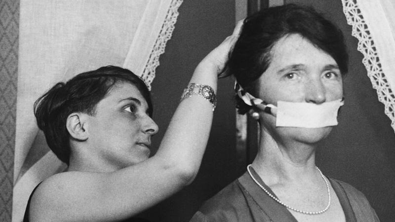 Uma mulher coloca uma m&aacute;scara no rosto de Margaret Sanger em Boston em 17 de abril de 1929
