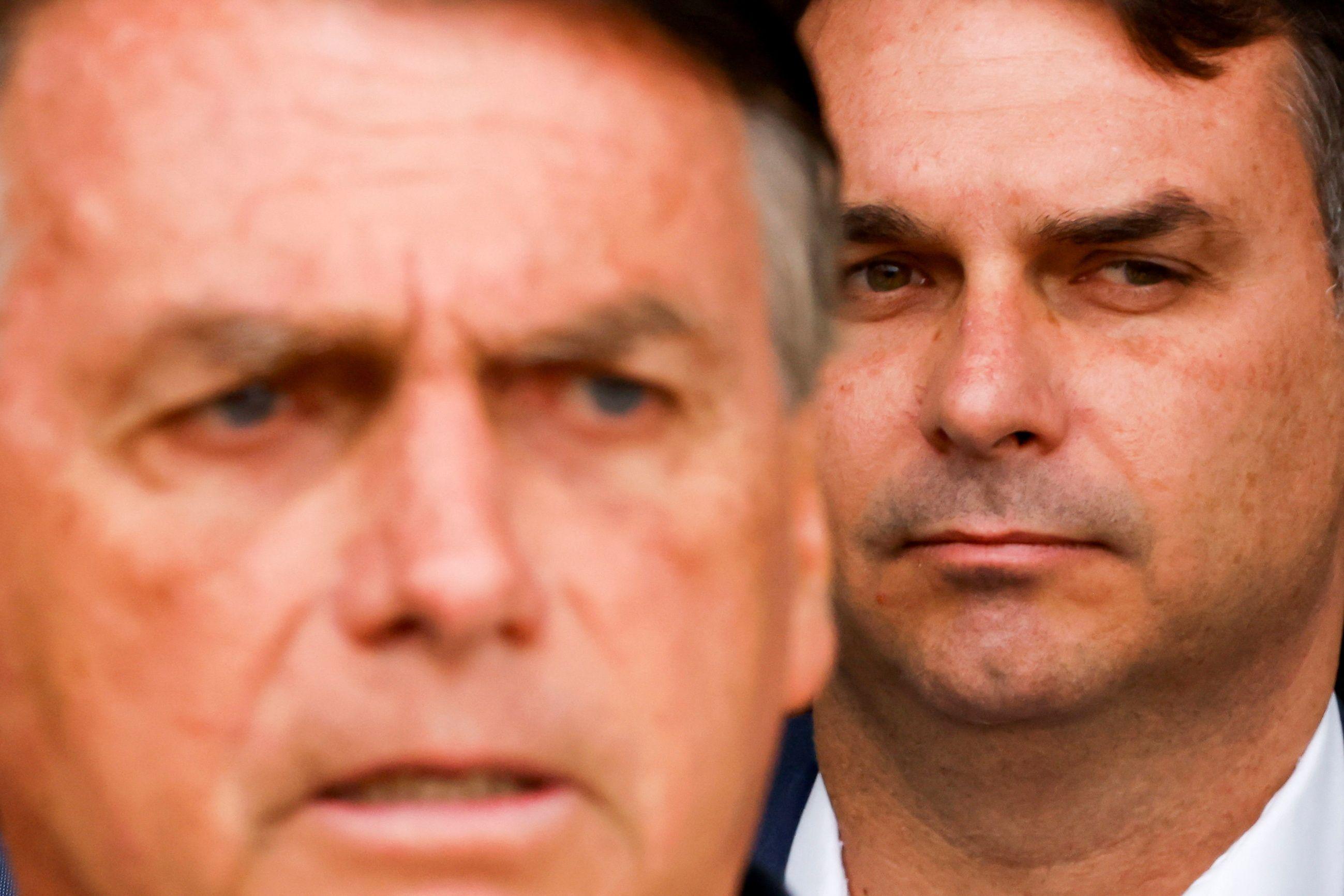 Imagem do rosto de Jair Bolsonaro levemente desfocado em primeiro plano, com rosto de Fl&aacute;vio focado, ao seu lado, um pouco atr&aacute;s