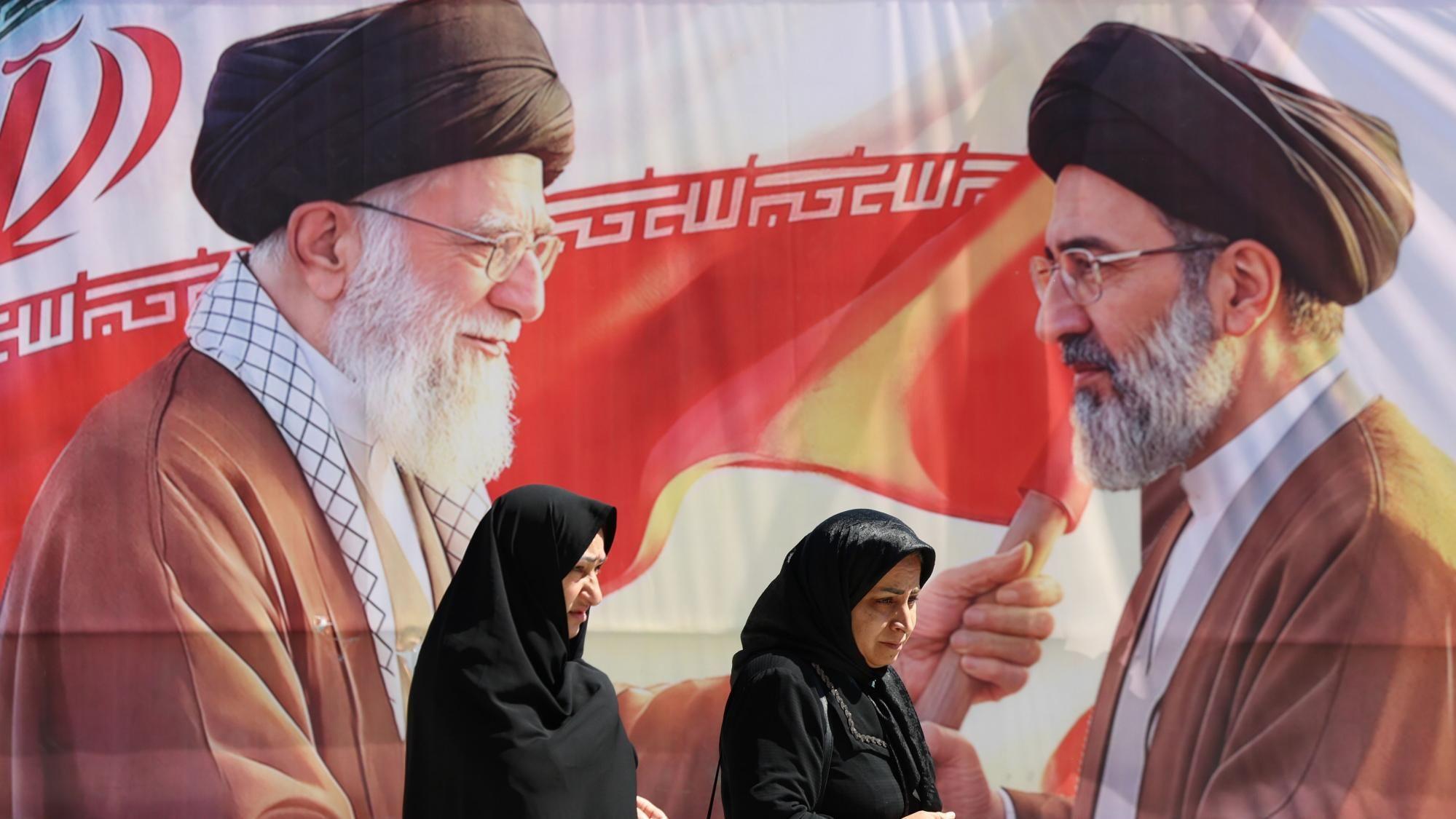 Mulheres iranianas passam por um painel com imagens do falecido l&iacute;der supremo do Ir&atilde;, o aiatol&aacute; Ali Khamenei (&agrave; esquerda), e de seu filho e sucessor no cargo, Mojtaba Khamenei (&agrave; direita), em Teer&atilde;, no Ir&atilde; (23/04/2026) 