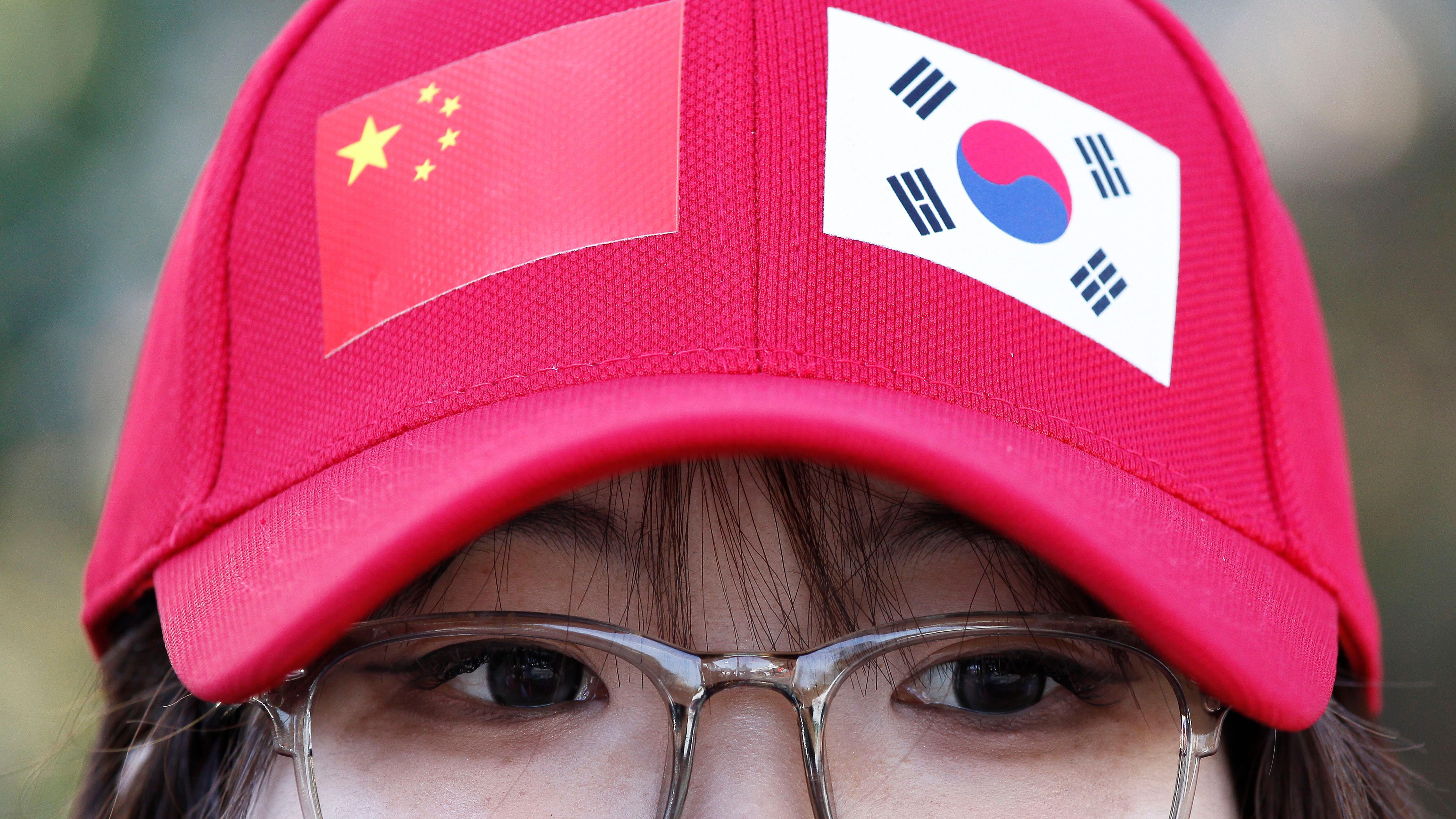 韓國慶尚南道金海國際機場外一位女生戴著貼有中國（左）、韓國（右）國旗的紅色鴨舌帽等候迎接習近平抵達（30/10/2025）