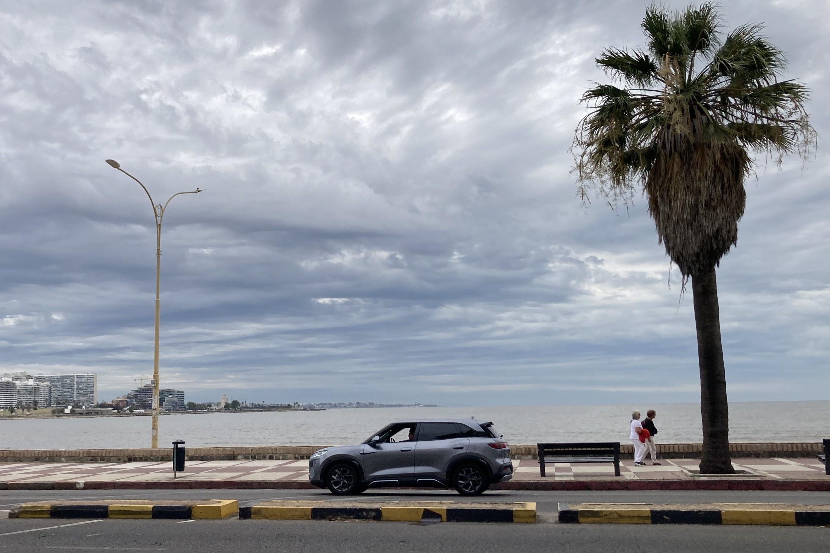 Carro el&eacute;trico ao lado de uma palmeira e duas pessoas, na avenida da praia em Montevid&eacute;u