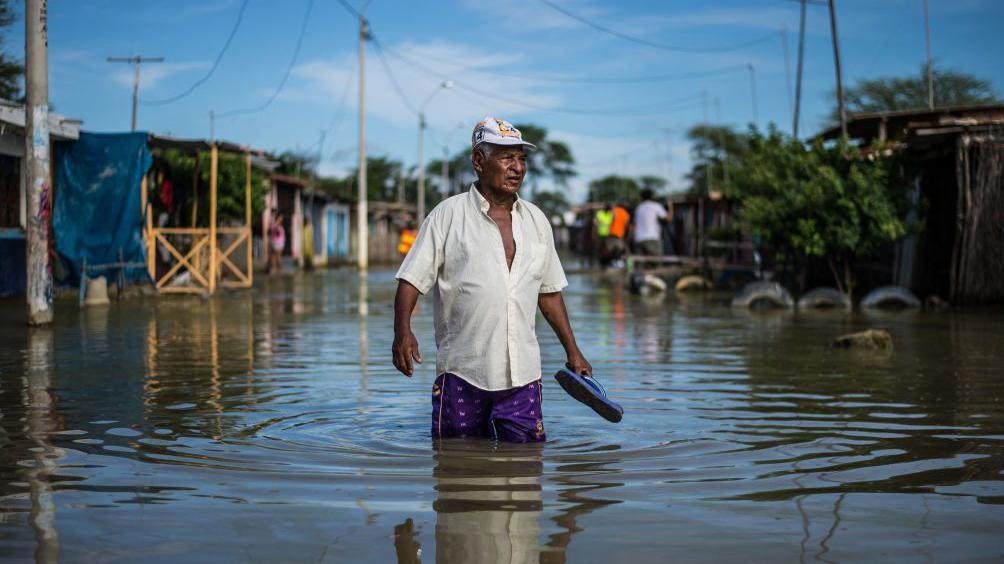 Un hombre camina con el agua por encima de las rodillas en una inundación por el fenómeno de El Niño en Perú
