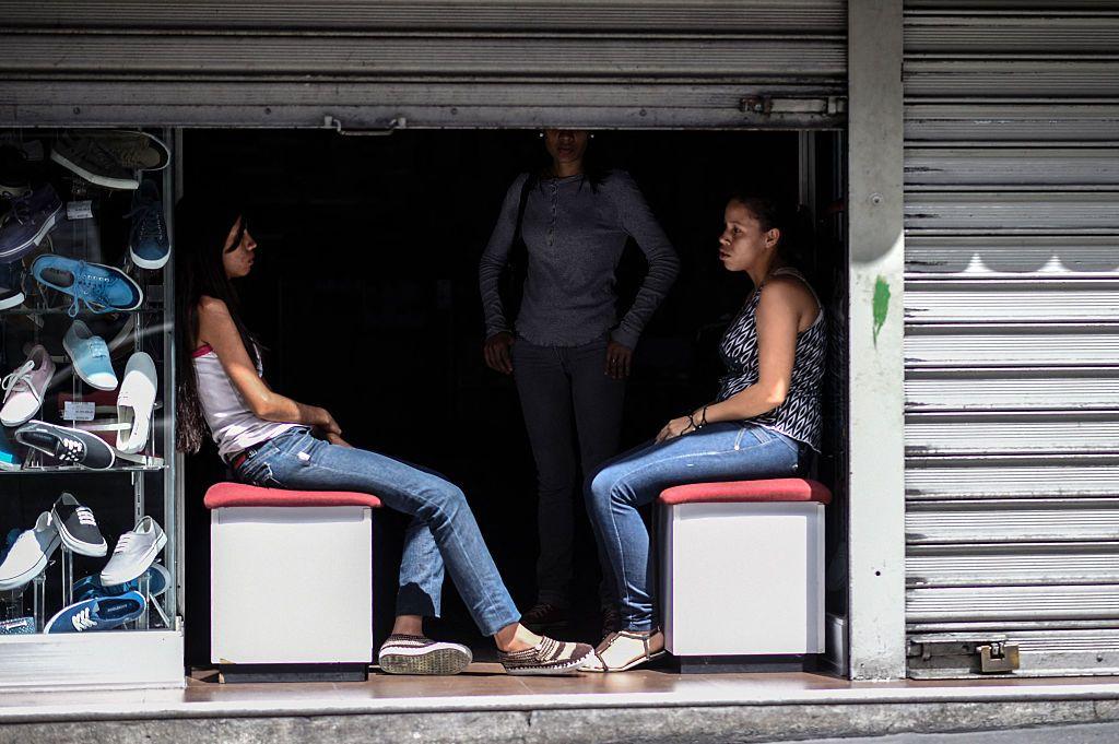 Empleadas de una zapatería aparecen en una fotografía sentadas a la entrada de un local a oscuras durante un corte de electricidad en Caracas.