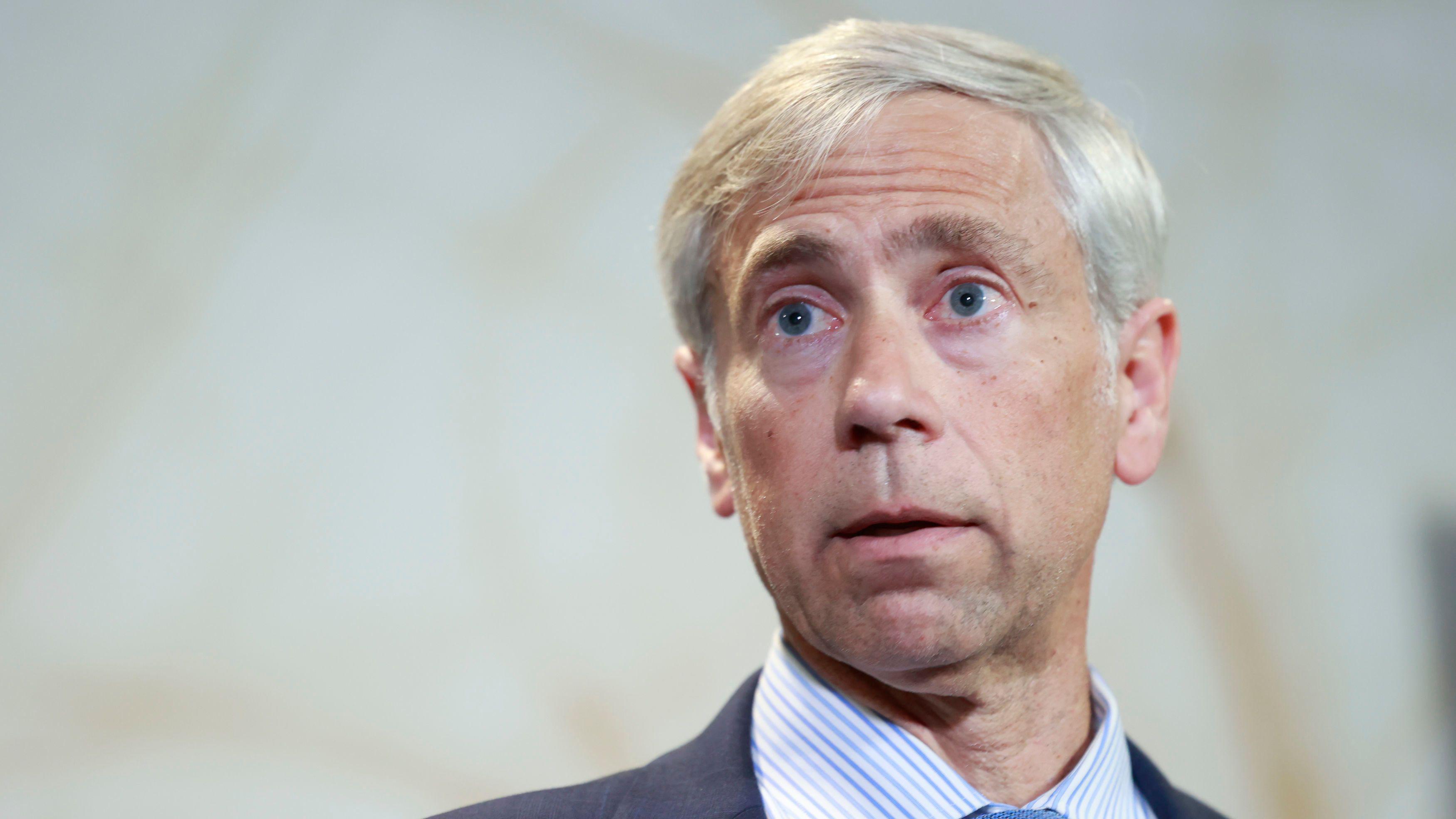 Barry Pollack com terno azul-marinho, camisa listrada azul e branca e gravata azul