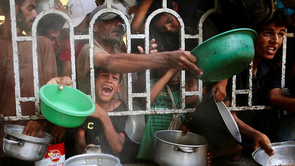 Varios palestinos se agolpan para recibir una comida caliente en un comedor social, al sur de la Franja de Gaza.