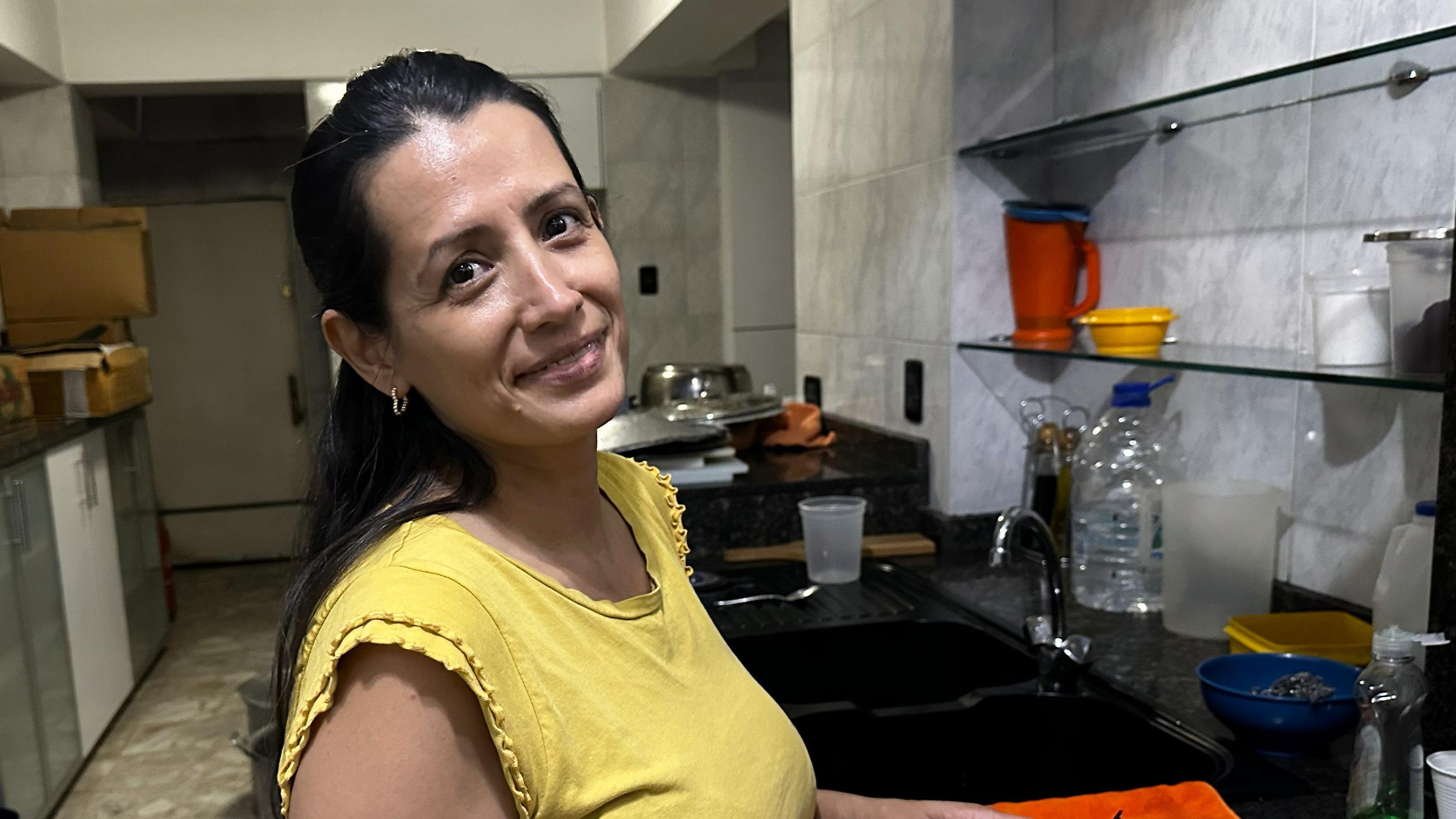 Crismary López sonríe a la cámara desde la cocina. Lleva una blusa amarilla.