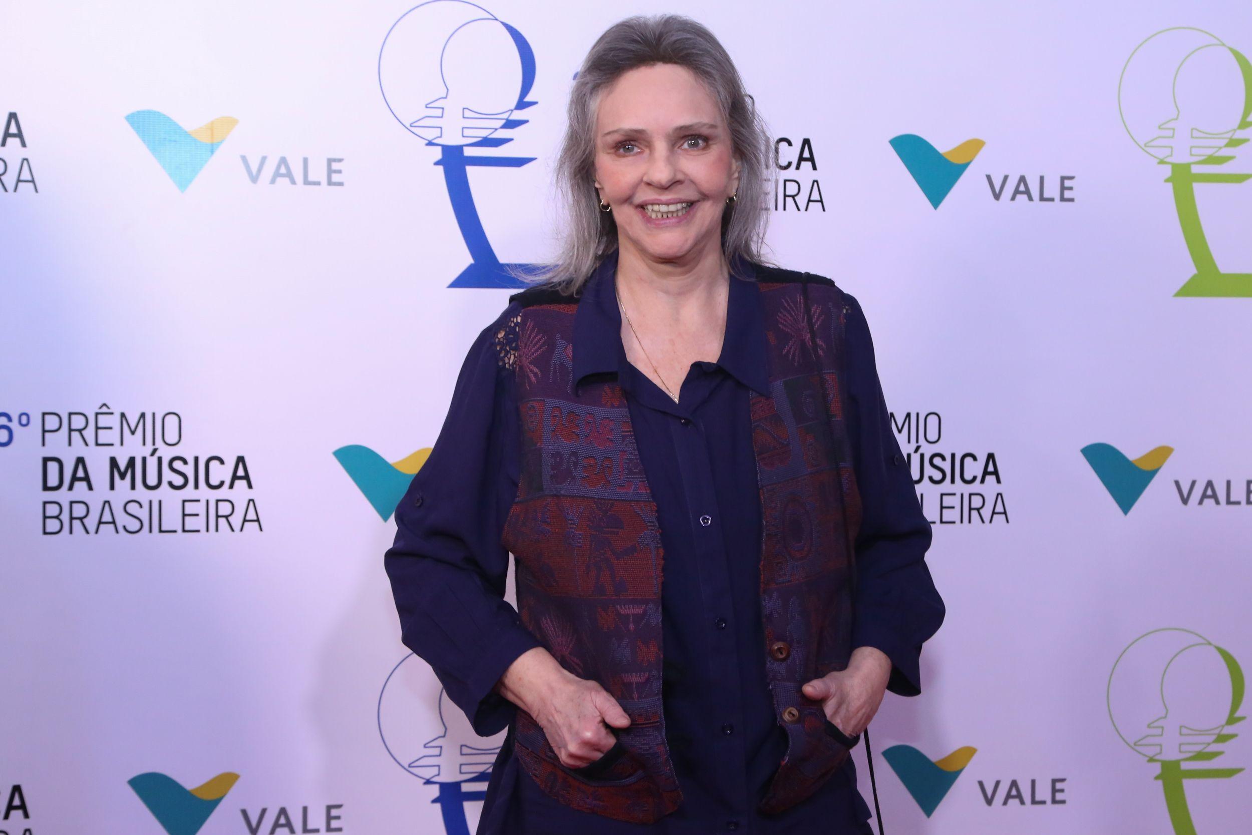 Ro Ro em frente a painel de evento, sorrindo