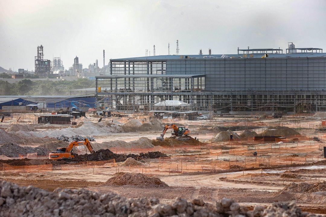 Obra da constru&ccedil;&atilde;o da f&aacute;brica da BYD em Cama&ccedil;ari com escavadeiras, pilhas de materiais e estruturas met&aacute;licas ao fundo
