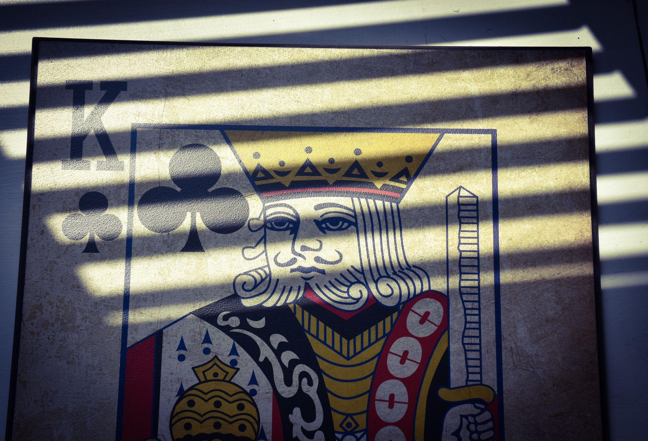 Tarjeta de rey de tréboles entre la luz y la sombra que reflejan unas rejas.