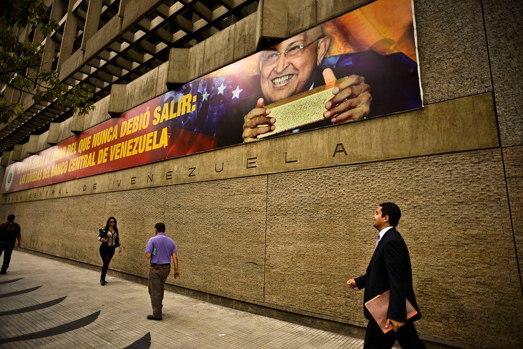 Unas personas caminan frente a la sede del BCV, en Caracas y en su fachada una foto de Chávez con un lingote de oro.