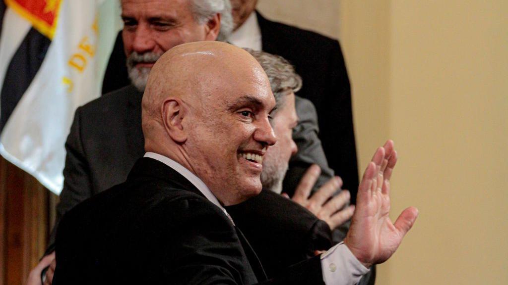 Ministro do STF Alexandre de Moraes faz aceno com a mão e sorri